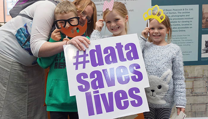 Three children and an adult standing together holding a #datasaveslives sign.