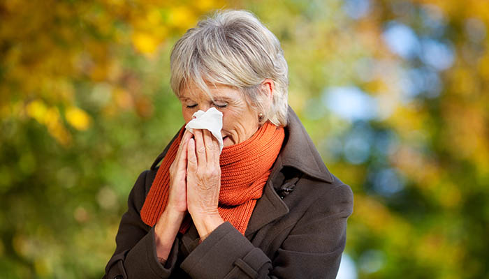 A woman walking outside, sneezing due to allergies.