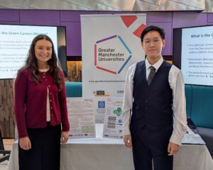 Two individuals standing beside a display for Greater Manchester Universities