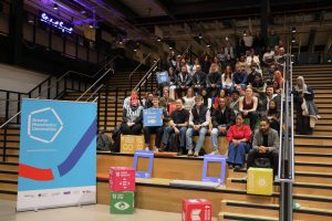 Large group of people sitting on staircase with colourful cubes and Greater Manchester Universities Banner Stand