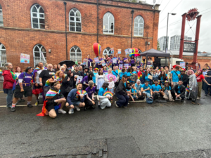 Staff group pose outdoors in colourful clothes with Pride Banners and Rainbow Banners